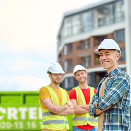 Tre byggjobbare framför Sortera-container
