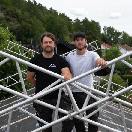 Två män på ett tak med byggnadsställningar